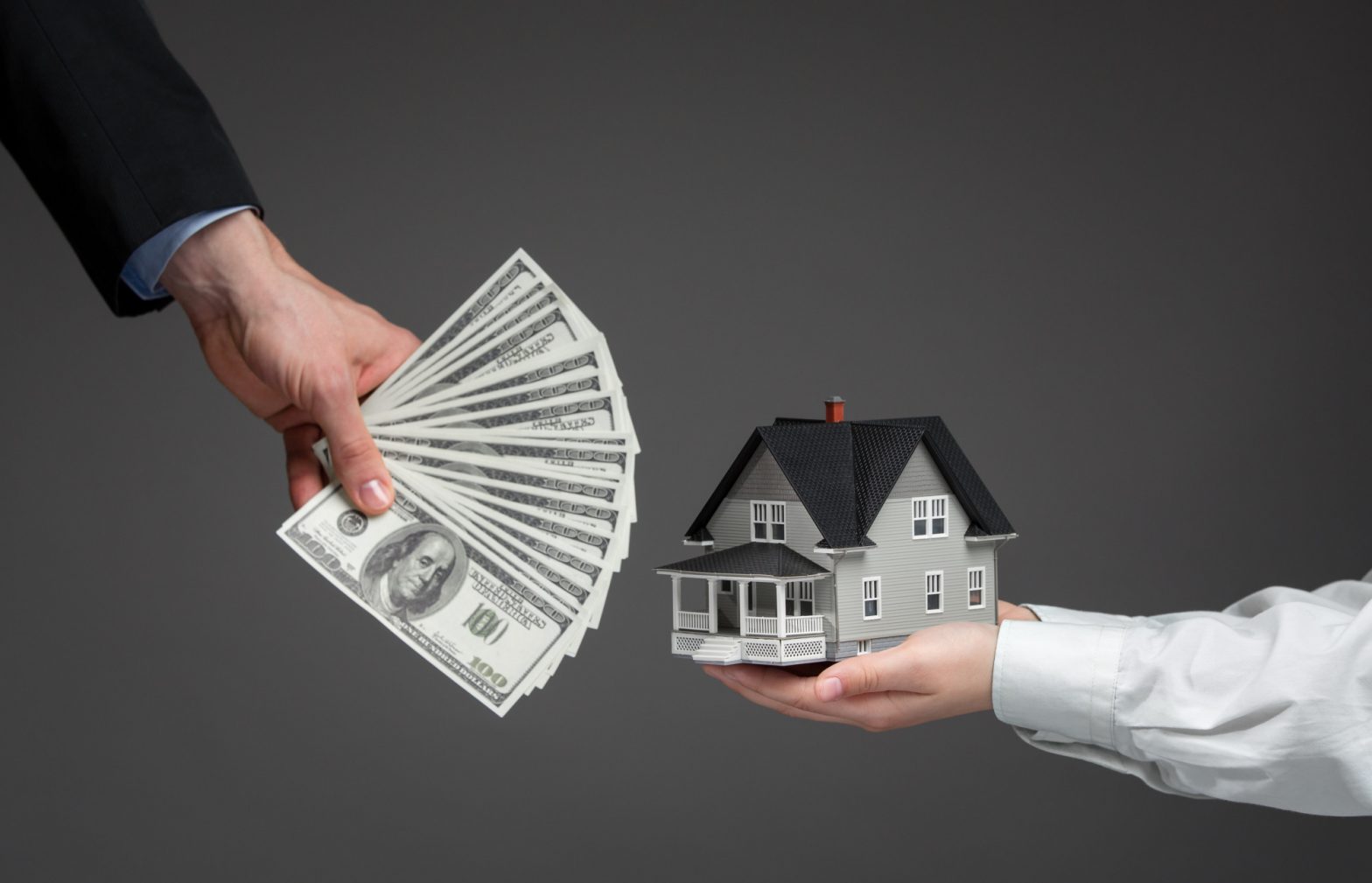 Close up of hands giving house model to other hands with money. Concept of real estate and deal